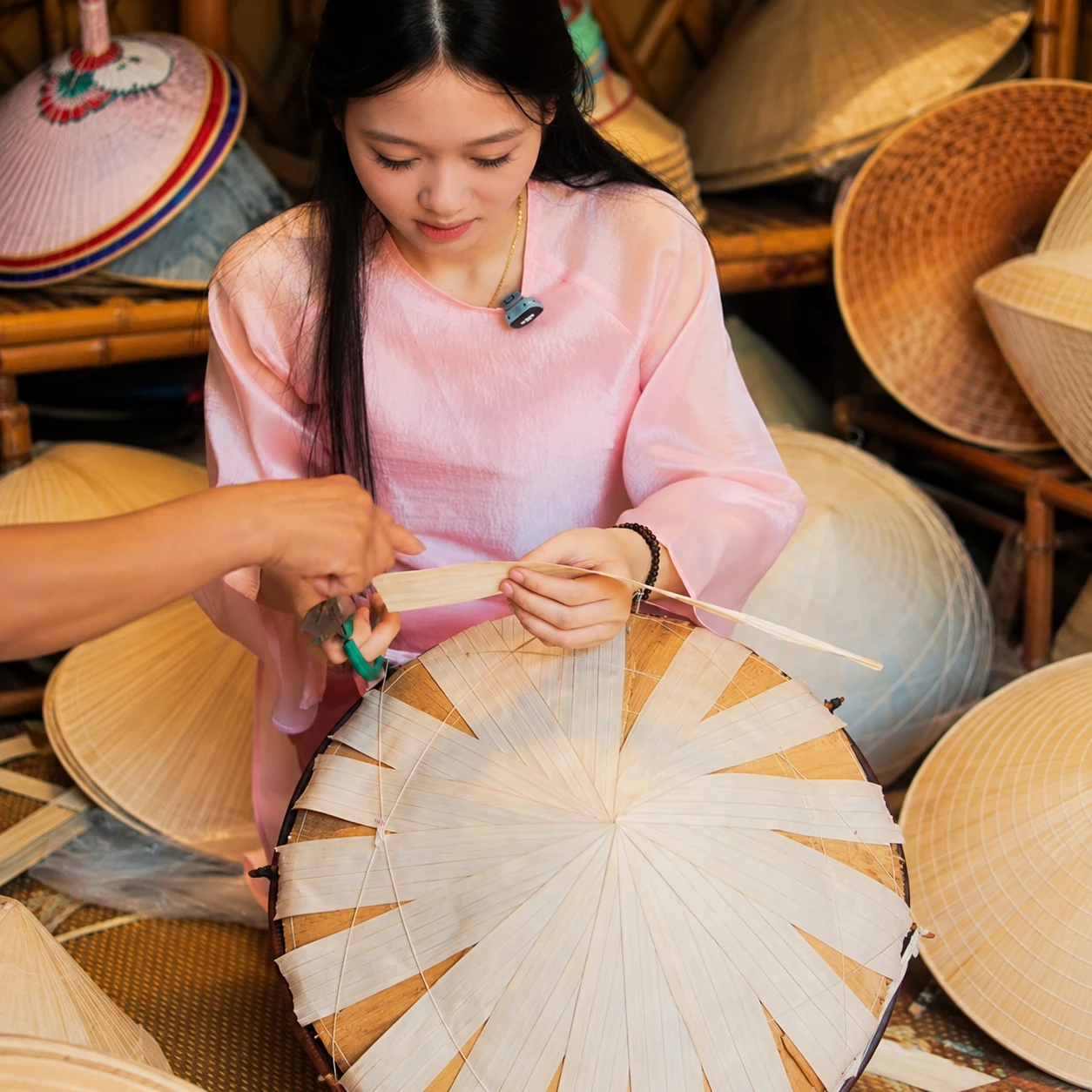 Cô gái mặc áo dài hồng tập xếp lá trên khuôn nón, có bàn tay hướng dẫn bên cạnh